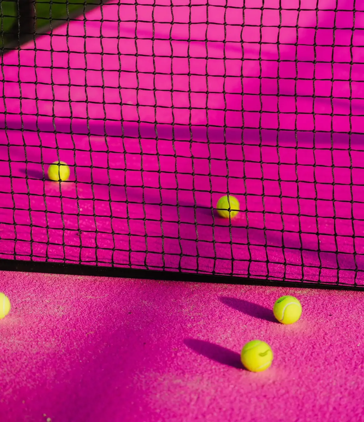 Padel balls on a pink court beside the net at Padel Tropical