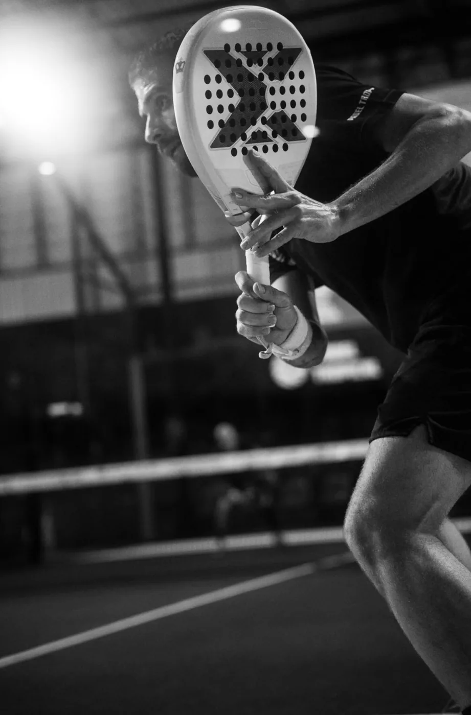 Black and white action shot of a padel player serving at Padel Tropical